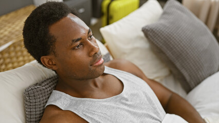Fototapeta premium A relaxed young black man lounging in a modern bedroom, contemplating in a well-furnished interior.