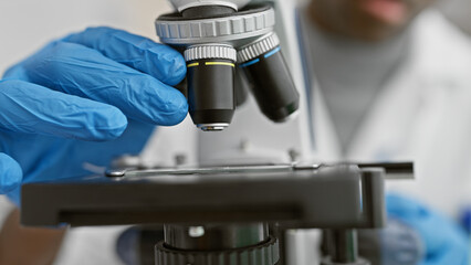 Close-up of a male scientist adjusting a microscope in a laboratory setting, depicting research and healthcare.