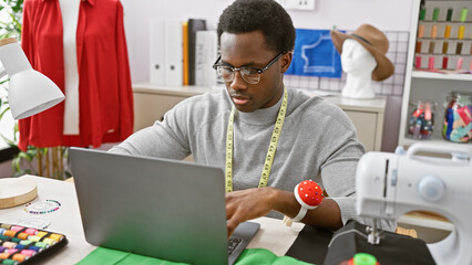 A focused african american man designs clothing in a modern atelier with sewing equipment.