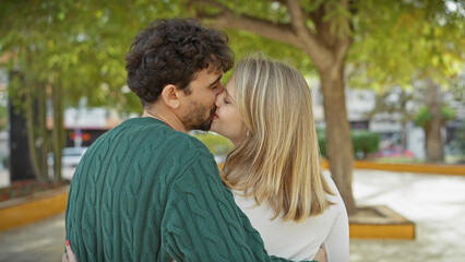 Obraz premium A man and woman share a tender kiss in a lush outdoor park setting, evoking love and companionship.