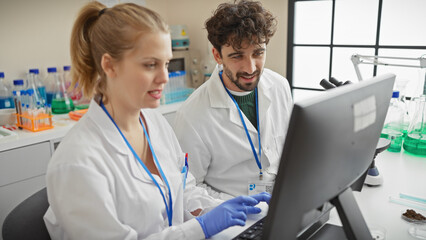 Two scientists, a man and a woman, working together in a laboratory setting, using a computer indoor.