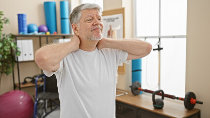 Middle-aged man with grey hair experiencing neck pain in a physiotherapy clinic room.