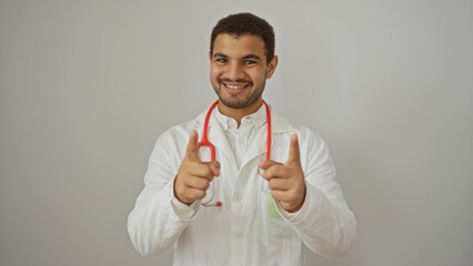 Young male doctor pointing at the camera with both hands, wearing a white coat and stethoscope, against an isolated white background, appearing confident and approachable.