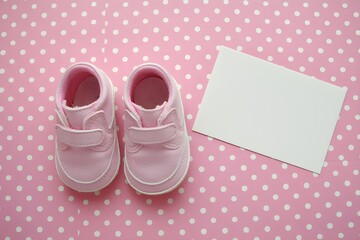 Pink baby shoes against polka dot background, blank white card beside them