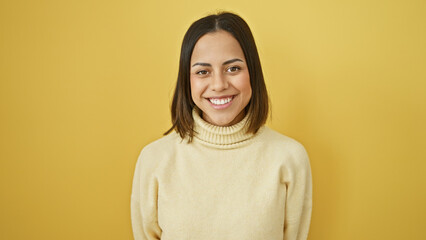 Fototapeta premium A cheerful young hispanic woman with a beautiful smile poses in an ivory sweater against a yellow isolated background.