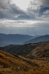 Majestic mountain landscape at twilight showcasing autumn colors in the valley below. A breathtaking view of layered mountain featuring vibrant autumn foliage and soft clouds.
