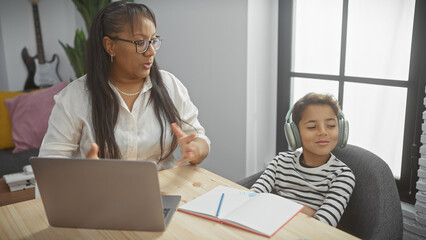 A woman teaches a boy wearing headphones at a laptop in a living room, exemplifying family education and home schooling.