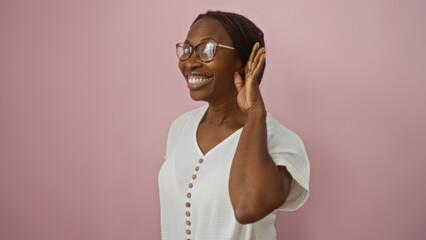 African american woman smiling and holding hand to ear over an isolated pink background.