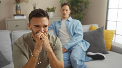 Man crying in living room with another man sitting on sofa in the background showcasing a moment of...