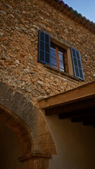 Fototapeta premium Stone building facade with arched entrance and blue shutters on a window under a bright sky