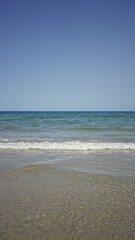 Tranquil beach with gentle waves meeting the sandy shore under a clear blue sky creating a peaceful coastal scene perfect for relaxation.
