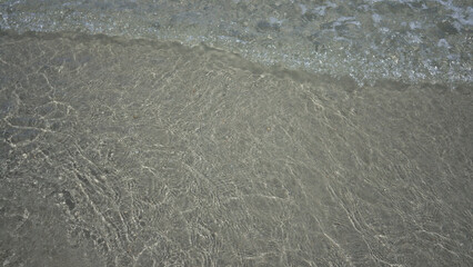 Clear water lapping gently on a sandy beach creates tranquil wave patterns at the seaside, capturing the essence of a calm summer day outdoors near the sea.