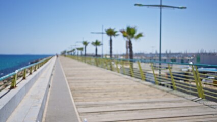 Blurred boardwalk with palm trees lined up along an outdoor pathway by the seaside under a clear blue sky