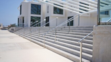 Fototapeta premium Defocused, outdoor, blurry image of modern, white building exterior with glass, railings and multiple steps on a sunny day.