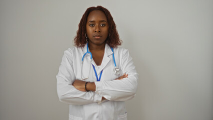 Young african american female doctor crossing her arms confidently, isolated against a white background, showcasing professionalism and dedication in the medical field.