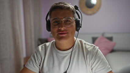 Young man wearing headphones and glasses sitting in a cozy living room, highlighting his handsome...