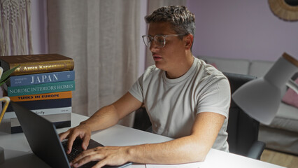 Young man typing on laptop in home living room with books stacked nearby exemplifies a casual, indoor setting