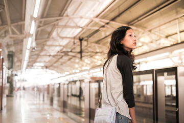 An Asian teenage girl waiting alone for the arrival of commuter train at subway station platform
