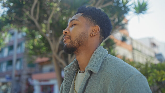 African american man enjoys a serene moment outdoors, framed by greenery in a peaceful urban garden setting. - Powered by Adobe
