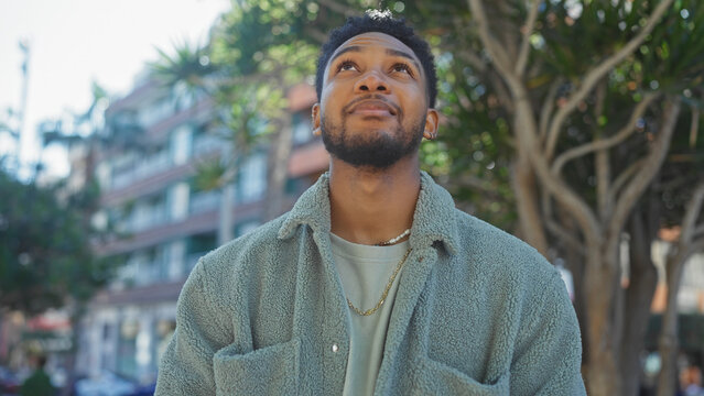 A contemplative african american man standing outdoors on a city street, exuding confidence and style.