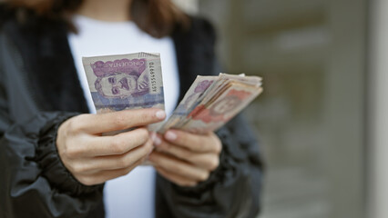 Young hispanic woman counts colombian pesos on a bustling city street.