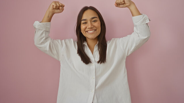 Beautiful young hispanic woman in white shirt over isolated pink background making a strong gesture with her arms, smiling confidently and looking at the camera