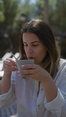 A young woman enjoys a peaceful moment sipping coffee outdoors with natural light highlighting her calm demeanor and casual attire.