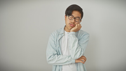 A young asian man with glasses stands bored against a white isolated background, portraying a casual and modern vibe.