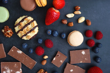 Macarons, chocolate, cookies, berries and various nuts on dark blue background. Top view.