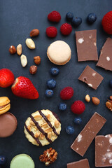 Macarons, chocolate, cookies, berries and various nuts on dark blue background. Top view.
