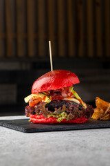 A gourmet burger with a striking red bun features fresh toppings like lettuce, avocado, and bacon....