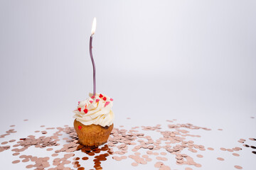 Delicious festive cupcake with burning candle, heart sprinkles on colorful background