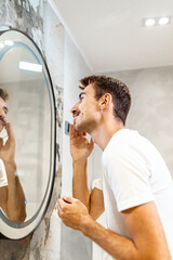 Young man trims his mustache with scissors in the bathroom in front of the mirror.