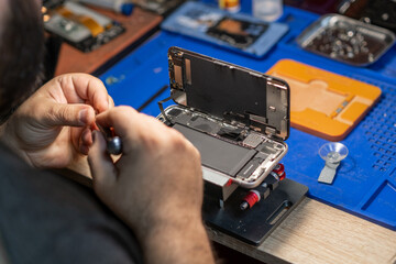 A technician focuses on replacing a smartphone battery while surrounded by tools in a repair shop