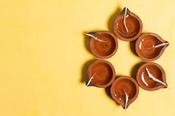 Happy Diwali - Hindu traditional clay diya arrangement for Diwali festival of lights celebration on yellow background.