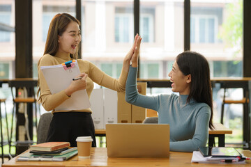 Two Asian woman colleagues give each other a high five, Successful business team working together...