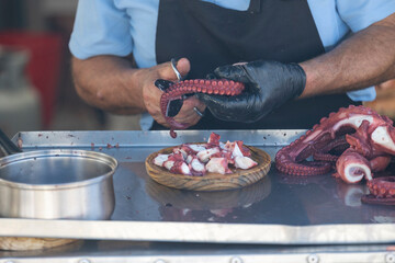 A person is skillfully slicing fresh octopus tentacles at a street market stall, showcasing culinary expertise and attention to detail in seafood preparation.