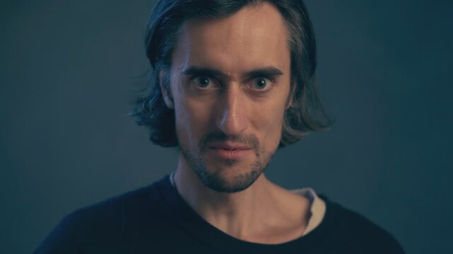 a young man with long hair, large expressive eyes, European appearance, a crazy look, looking intently without taking his eyes off, looking at the camera, insanely dangerously serious