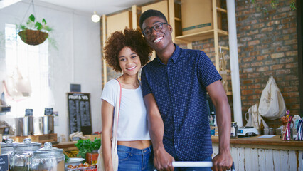 Portrait Of Young Couple Pushing Trolley Shopping In Sustainable Plastic Free Grocery Store
