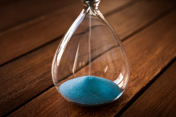 Hourglass containing blue sand on a rustic wooden board