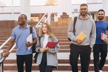 Obraz premium Diverse Group of College Students Walking Together on Campus Stairs Smiling and Holding Notebooks