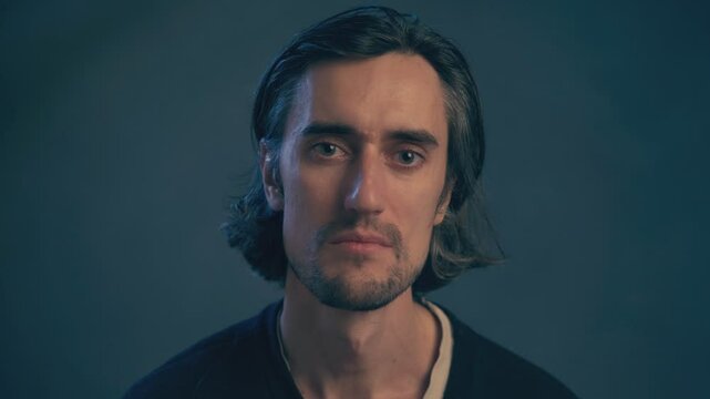 a young man with long hair, large expressive eyes, European appearance, looks soulfully into the frame, eyes sparkle with tears inside, fullness sends a farewell kiss, smiles with light sadness