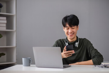Fototapeta premium Young Boy Studying Online with Laptop and Smartphone in Modern Home Setting, Smiling and Engaged in Learning