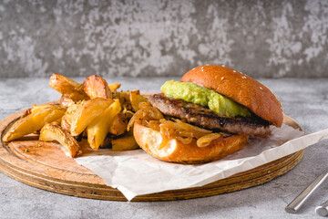 Burger with caramelized onion and avocado on a wooden cutting board