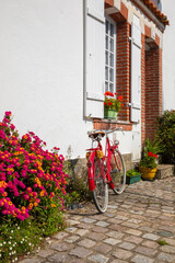 Vieux vélo rouge au pied d'une maison fleurie dans les rues d'un village de Vendée en France.