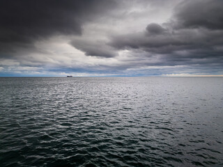 A panoramic view of a vast ocean under a dramatic, overcast sky. A distant ship on the horizon...