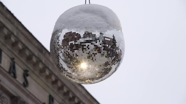 Silver disco ball is spinning in a circle, there is white snow on top, and the sun is shining on the sides of the ball (185)