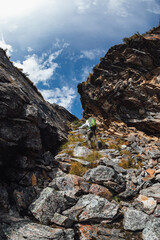 Backpacking woman climbing up on steep cliff edge at high altitude mountains top