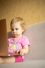 Cute girl sitting on bed watching something on laptop. Children's screen time.