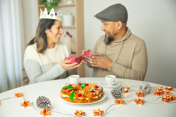 A smiling woman wearing a traditional Three Kings' Day crown exchanging gifts with her partner.
